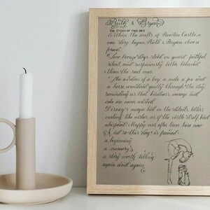 May include: A framed print with handwritten text and a sketch, next to a beige ceramic candle holder with a white candle. The print has a light wood frame and the text is in a cursive font.