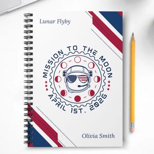 May include: A white spiral-bound notebook with a space-themed design. The cover features the text "Lunar Flyby" and "Mission to the Moon" with an astronaut graphic. The date "April 1st, 2026" is also displayed. A yellow pencil rests beside the notebook.