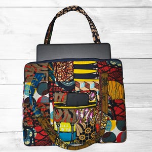 May include: A rectangular patchwork tote bag featuring a vibrant mix of geometric and circular patterns in yellow, red, blue, brown, and black. The bag includes a top handle, a zippered front pocket containing a black smartphone, and a laptop.