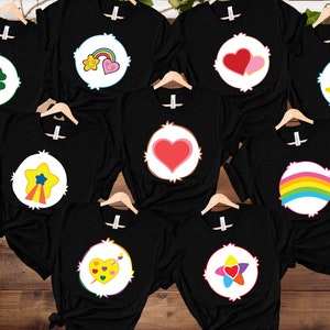 May include: Eight black t-shirts with different Care Bear characters printed on the front. The characters include a rainbow, a heart, a star, a clover, a music note, and a heart with a rainbow.