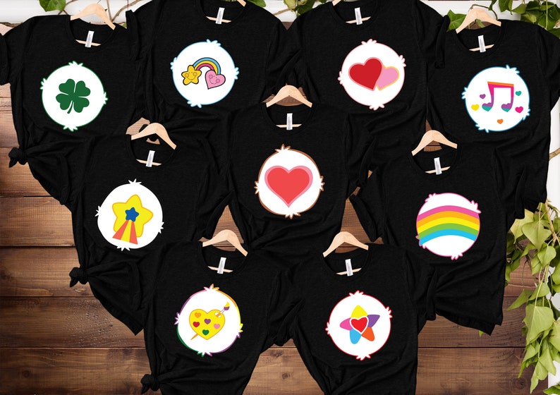 May include: Eight black t-shirts with different Care Bear characters printed on the front. The characters include a rainbow, a heart, a star, a clover, a music note, and a heart with a rainbow.