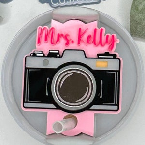 May include: A pink and gray camera-themed acrylic tumbler lid with the text "Mrs. Kelly" in pink lettering.