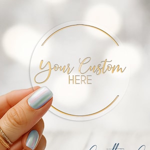 May include: Clear gloss labels with a choice of foil finish. The round sticker has a gold border and the words "Your Custom HERE" in gold script. The Critter Cup customs logo is in the bottom right corner.