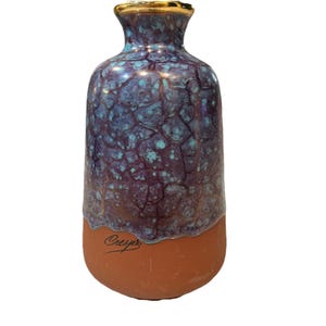 May include: A blue and purple ceramic vase with a gold rim and a crackled glaze. The vase has a terracotta base with the word "Crepus" written in cursive.