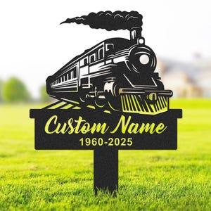 Könnte beinhalten: Schwarze Metallsilhouette einer Dampflokomotive mit Rauch aus dem Schornstein. Der Zug befindet sich auf einem Gleis mit einem Schild darunter, auf dem "Custom Name 1960-2025" steht.