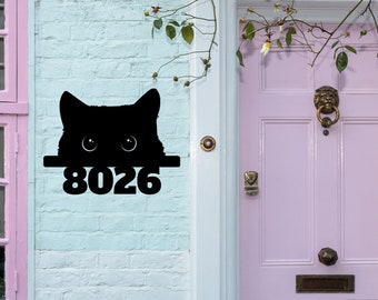 May include: Black silhouette of a cat peeking over a sign with the house number 8026. The sign is mounted on a white brick wall with a pink door to the right.