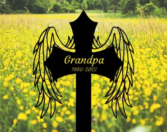 May include: Black metal cross with angel wings and the text "Grandpa 1950-2022" in yellow lettering, set against a background of yellow wildflowers.