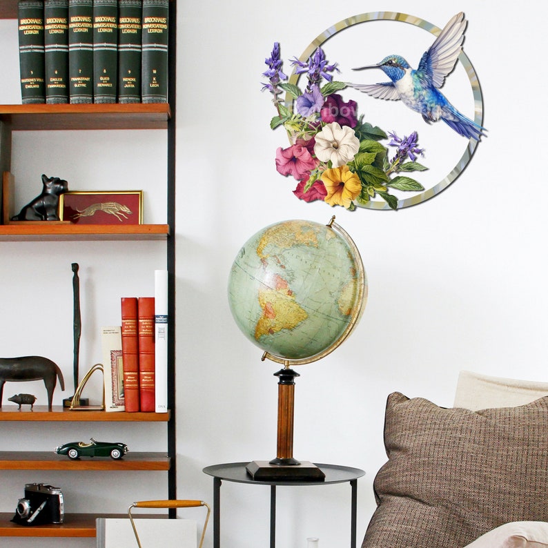 May include: A vintage globe with a wooden stand sits on a black table next to a brown couch. A wall decal with a hummingbird and flowers is on the wall behind the globe.