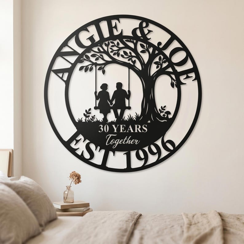 Puede incluir: Un letrero de pared circular de metal negro con la silueta de una pareja en un columpio bajo un &aacute;rbol. El texto dice ANGIE & JOE, 30 YEARS Together y EST 1996. El dise&ntilde;o est&aacute; cortado en una sola pieza de metal con acabado negro mate.