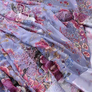 Op de afbeelding: Een vloeiende stof met een bloemenpatroon in tinten lavendel, roze en blauw. Het ontwerp toont gedetailleerde botanische illustraties van bloemen en bladeren, wat een zachte, romantische esthetiek creëert. De stof heeft een delicate, transparante kwaliteit.