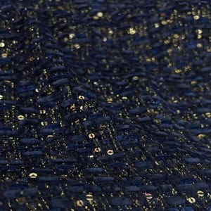 Puede incluir: Tela azul marino con lentejuelas doradas tejidas en toda la tela. La tela tiene una apariencia texturizada, similar al tweed.