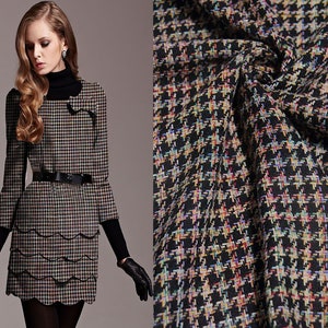 May include: A black and white houndstooth patterned dress with a scalloped hemline. The dress has a black belt and long sleeves.