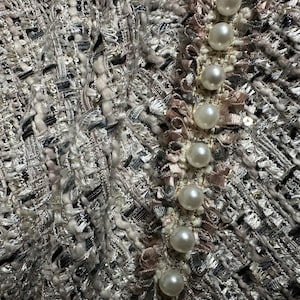 May include: Close-up of a silver and white tweed fabric with a row of pearl-like buttons down the side.