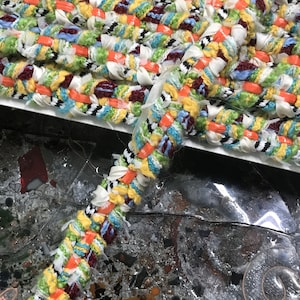 Puede incluir: Borde tejido multicolor con una mezcla de hilos amarillos, naranjas, verdes, azules, blancos y negros. El borde es texturizado y tiene un aspecto ligeramente deshilachado.