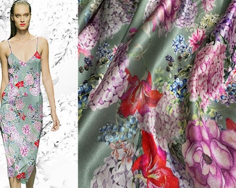 Op de afbeelding: Een groene zijden stof met een bloemenprint met roze, rode en blauwe bloemen. De stof heeft een zachte, vloeiende textuur.