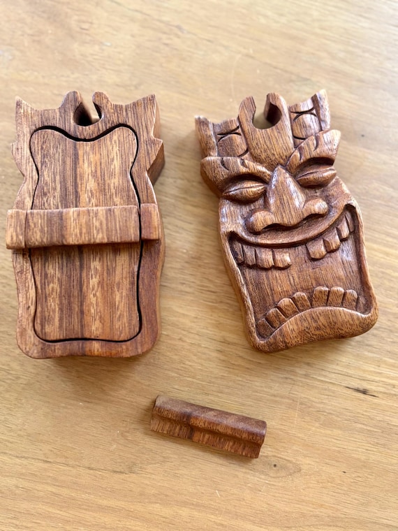 A hand-carved Tiki-themed wooden puzzle box — the specific Hawaiian folk-art aesthetic and secret stash function make it a genuinely niche, conversation-starting piece.