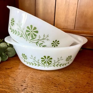 May include: Two white ceramic baking dishes with green floral designs. The dishes are stacked on top of each other.