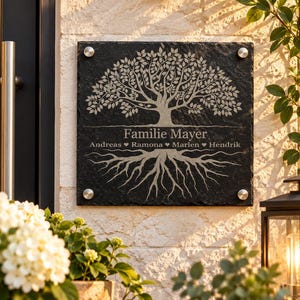 Peut inclure: Une plaque carrée en ardoise noire gravée d'un arbre avec des racines visibles. Le texte "Familie Mayer" est centré sous la canopée, suivi des prénoms "Andreas", "Ramona", "Marlen" et "Hendrik" séparés par des symboles de cœur.