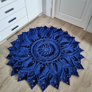 Peut inclure: Un tapis rond en crochet bleu foncé avec un motif floral. Le tapis présente un motif circulaire central entouré de formes complexes en forme de feuilles, créant une pièce texturée et décorative. Le tapis mesure environ 91 cm de diamètre.
