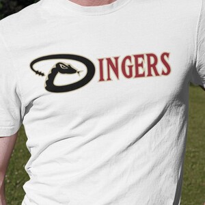 May include: White t-shirt featuring a black snake logo and the word "Dingers" in red lettering.
