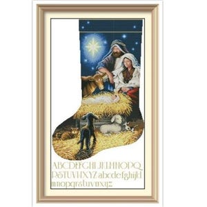 May include: A framed Christmas stocking cross-stitch design. The artwork depicts the Nativity scene with Mary, Joseph, baby Jesus, animals, and a bright star. The bottom of the stocking has the alphabet.