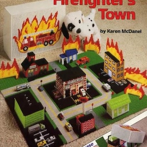 May include: Plastic canvas craft kit featuring a firefighter town scene with a fire truck, fire station, and buildings. The kit includes a fold-up case and is titled "Firefighter's Town" by Karen McDaniel.