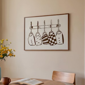 Puede incluir: Una impresión enmarcada con cinco diseños estilizados de utensilios de cocina marrones sobre un fondo crema. Los utensilios cuelgan de una barra horizontal. La escena incluye una mesa redonda de madera, un jarrón azul con flores amarillas y una silla de madera.
