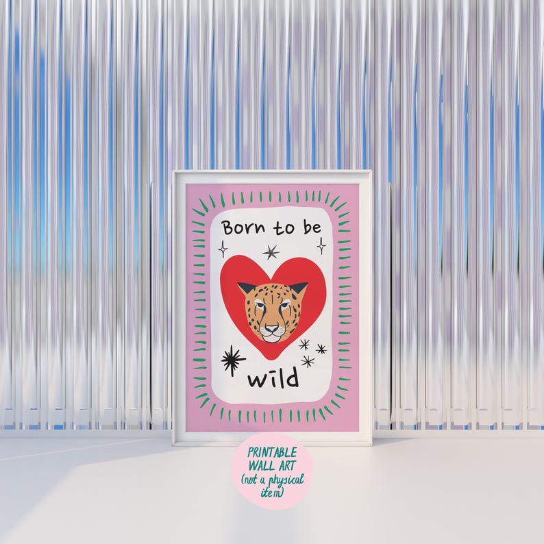 May include: A framed wall art print featuring a white background with a large red heart in the centre containing a leopard face. The text Born to be wild is written in black above and below the heart, surrounded by a pink border with green dashes.