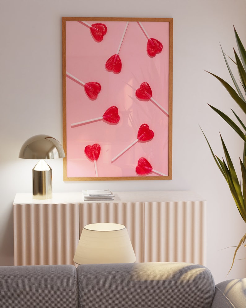 May include: A framed print of a pink background with multiple red heart-shaped lollipops on white sticks. The lollipops are arranged in a random pattern.