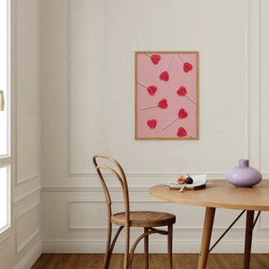 May include: A framed print of red heart-shaped lollipops on pink sticks arranged on a pink background.