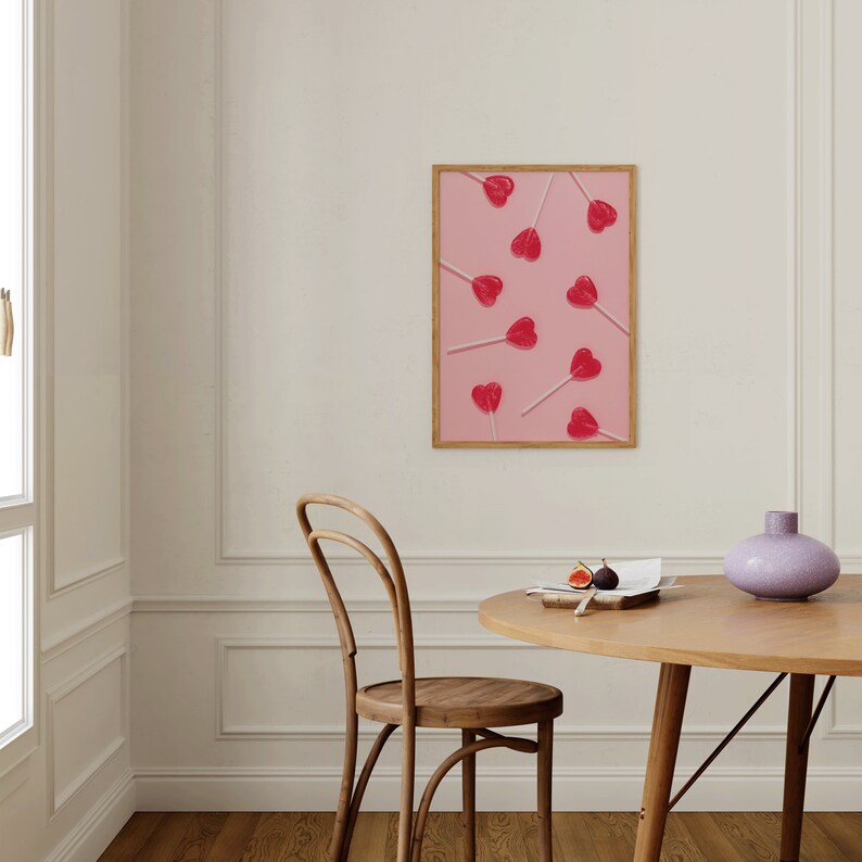 May include: A framed print of red heart-shaped lollipops on pink sticks arranged on a pink background.