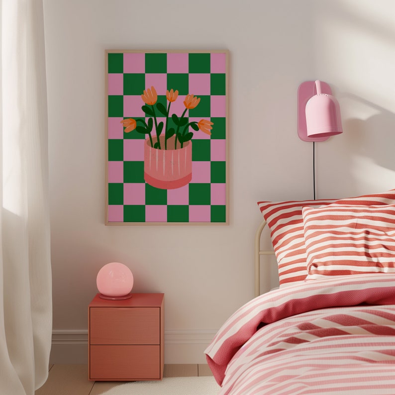 May include: A framed art print featuring a pink and green checkered background. A pink pot with orange flowers sits in the center. The artwork is displayed above a nightstand and bed with pink and white striped bedding.
