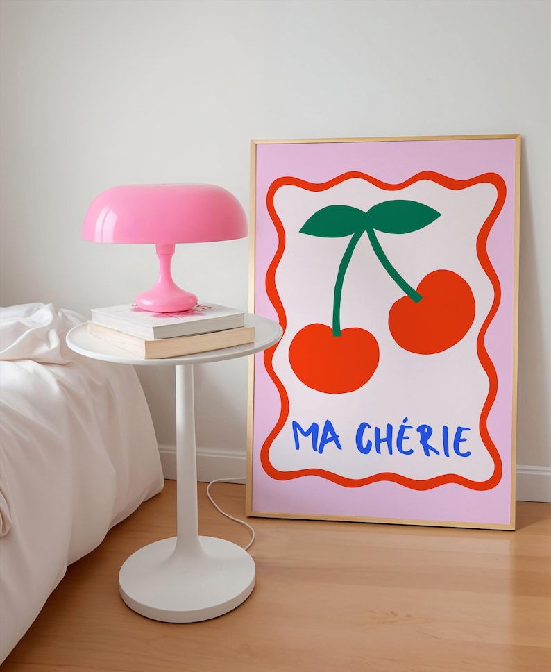 May include: A pink and gold framed print with a pink background. The print features two red cherries with green stems and leaves. The text "MA CH&Eacute;RIE" is written in blue below the cherries.