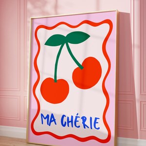 May include: A pink and white poster with a red border features a pair of red cherries with green stems and leaves. The text "MA CH&Eacute;RIE" is written in blue letters at the bottom of the poster.