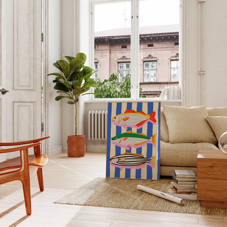 May include: A colorful artwork featuring three stylized fish against a blue and white striped background. The fish are in shades of red, green, and yellow, with pink and black details. The artwork is displayed in a bright, airy room.
