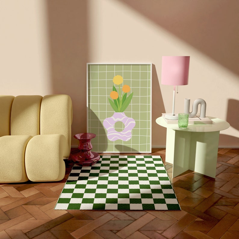 May include: A room scene with a yellow sofa, a green and white checkered rug, and a framed art print with a floral design. A pink lamp and a small side table with a green glass and decorative object are also present. A red vase is on the floor.