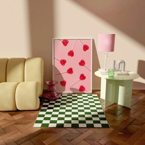 May include: A green and white checkered rug in front of a yellow couch. A framed print with pink hearts on sticks is on the wall behind the couch. A pink lamp with a white base is on a light green side table.