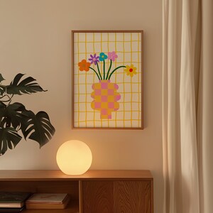 May include: A framed wall art print featuring a checkered pink and orange vase holding a bouquet of colorful flowers, including orange, purple, blue, pink, and yellow blossoms, set against a white background with a yellow grid pattern.