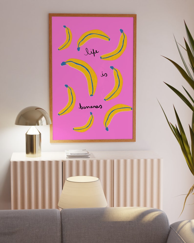 Może przedstawiać: Wydruk w ramie z r&oacute;żowym tłem i ż&oacute;łtymi bananami. Tekst "life is bananas" jest napisany na wydruku czarnym kolorem.