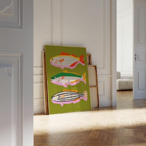 Puede incluir: Una impresi&oacute;n art&iacute;stica enmarcada con tres ilustraciones de peces estilizados. Los peces est&aacute;n representados en tonos rojos, verdes, amarillos y negros sobre un fondo verde. La obra de arte est&aacute; apoyada contra una pared en una habitaci&oacute;n con suelo de madera.