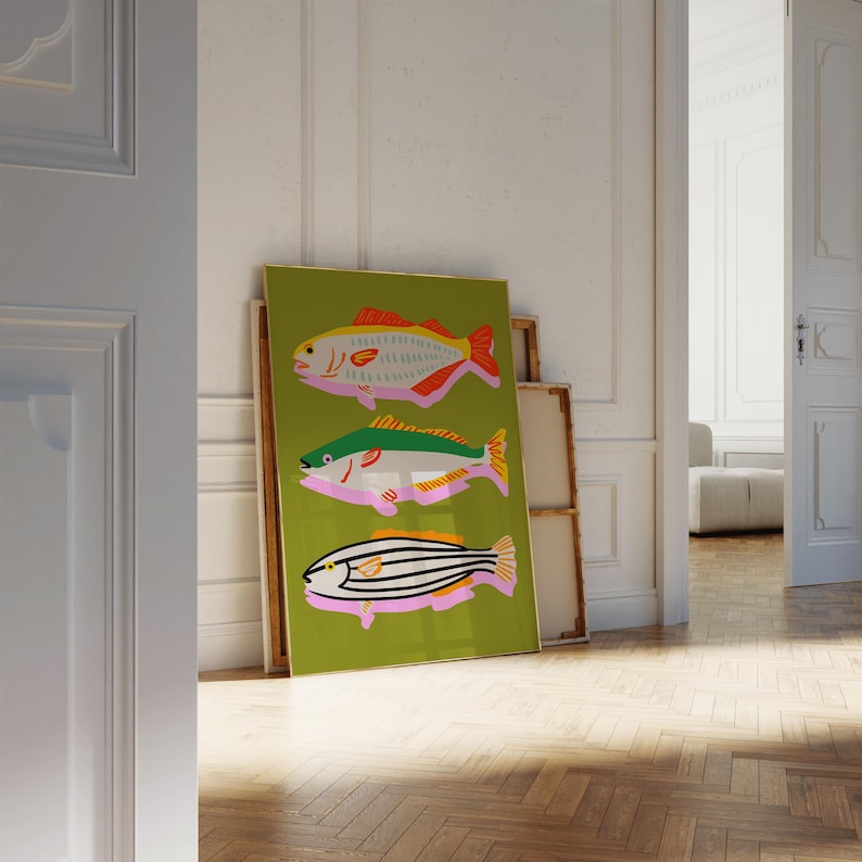 Puede incluir: Una impresi&oacute;n art&iacute;stica enmarcada con tres ilustraciones de peces estilizados. Los peces est&aacute;n representados en tonos rojos, verdes, amarillos y negros sobre un fondo verde. La obra de arte est&aacute; apoyada contra una pared en una habitaci&oacute;n con suelo de madera.