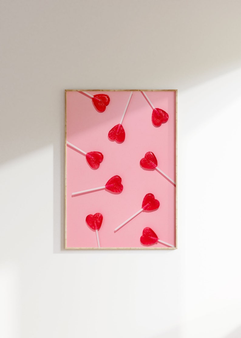 May include: A framed print with a pink background and multiple red heart-shaped lollipops on sticks.