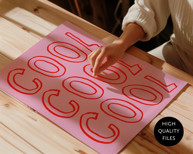 May include: A pink sheet of paper with the word "COOL" in red, outlined letters. The paper is on a wooden surface. A hand is touching the paper. A black circle with the words "HIGH QUALITY FILES" is in the bottom right corner.