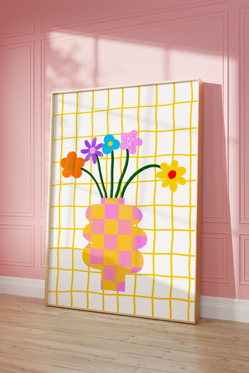 May include: A framed wall art print featuring a white background with a yellow grid pattern. A vase with a pink and yellow checkerboard design holds five colorful flowers in orange, purple, blue, pink, and yellow with green stems.