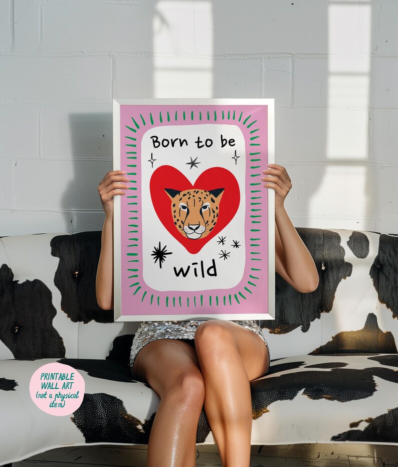 May include: A rectangular wall art print in a silver frame featuring a white background with a large red heart containing a leopard face. The text Born to be wild is printed in black. The border is pink with green dashes and black star accents.