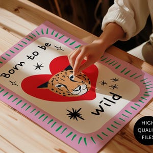 May include: A rectangular print featuring a cream-coloured centre with a red heart and a cheetah face illustration. The text "Born to be wild" is printed in black. The border is light pink with green dashes and black star accents.