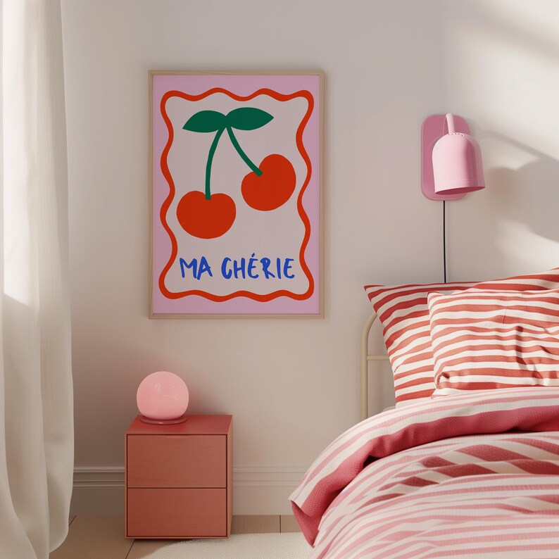 May include: A pink and white framed print with a red cherry illustration and the text "Ma Ch&eacute;rie" in blue and red letters. The print is hanging on a white wall above a red nightstand with a pink globe lamp.