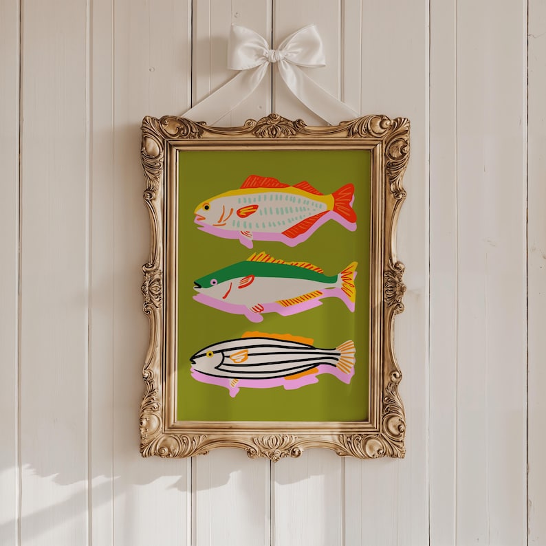 Puede incluir: Una impresi&oacute;n art&iacute;stica enmarcada con tres ilustraciones de peces coloridos sobre un fondo verde. Los peces son de color rosa, amarillo, rojo, verde y negro. El marco dorado ornamentado est&aacute; suspendido por una cinta blanca atada con un lazo.