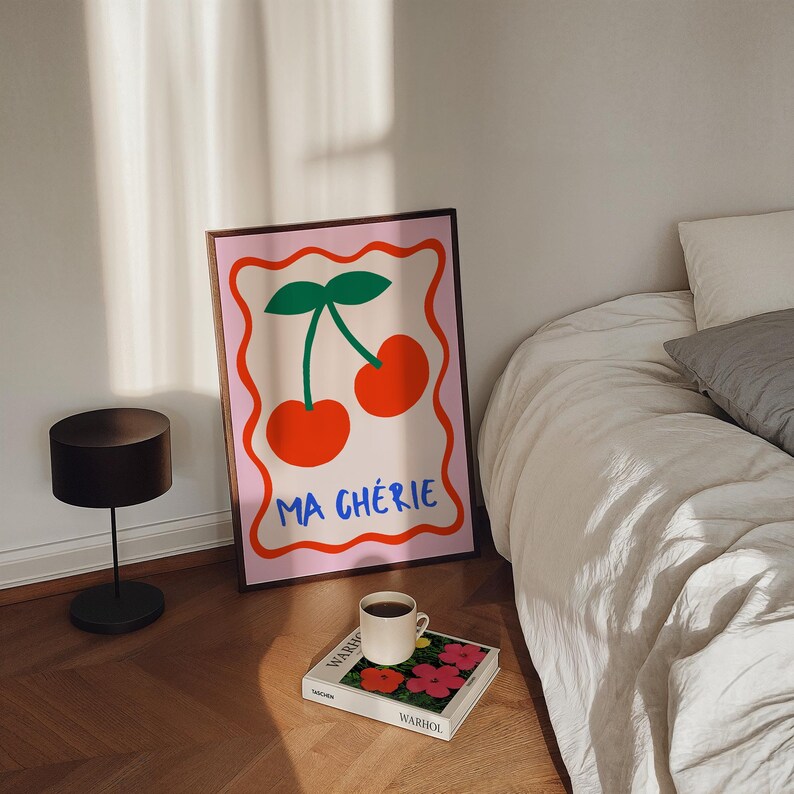 May include: A pink framed poster with a graphic illustration of two red cherries with green stems and leaves. The poster has the text "Ma Ch&eacute;rie" in blue and white lettering.