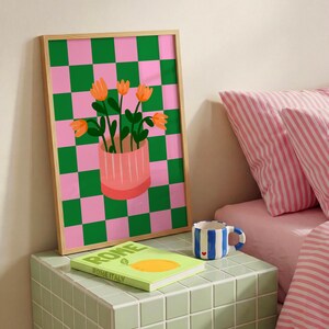 May include: A framed art print featuring a pink and green checkered background. The print showcases a pink vase with orange flowers. A green book with the word "ROME" is on a green tiled surface, along with a blue and white striped mug.